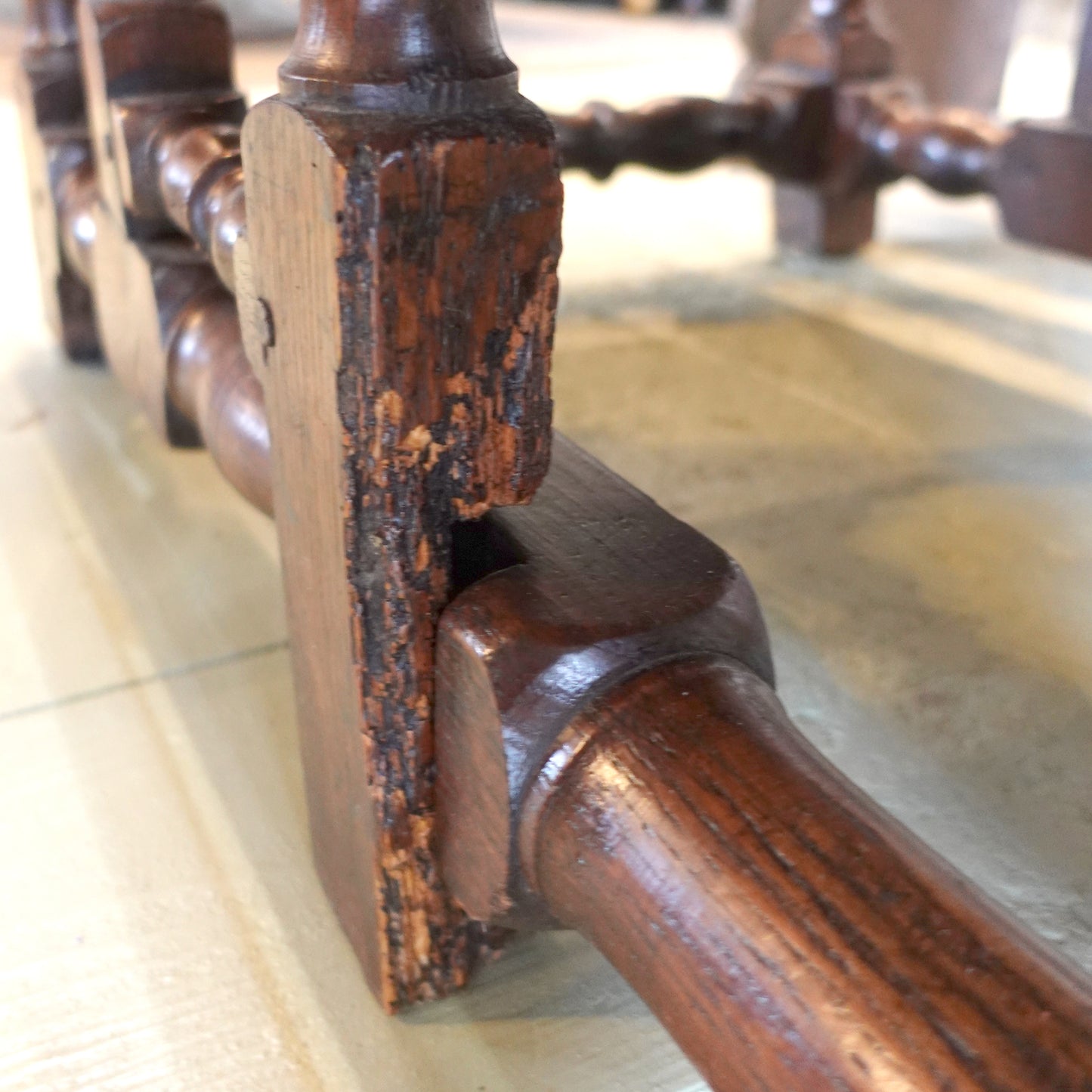 Close-up of a wooden chair leg with a worn finish on a tiled floor.