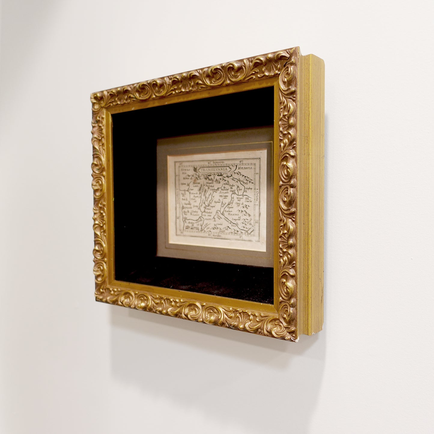 Decorative gold frame with a black mat holding an antique map of Dracula Transylvania on a white wall.