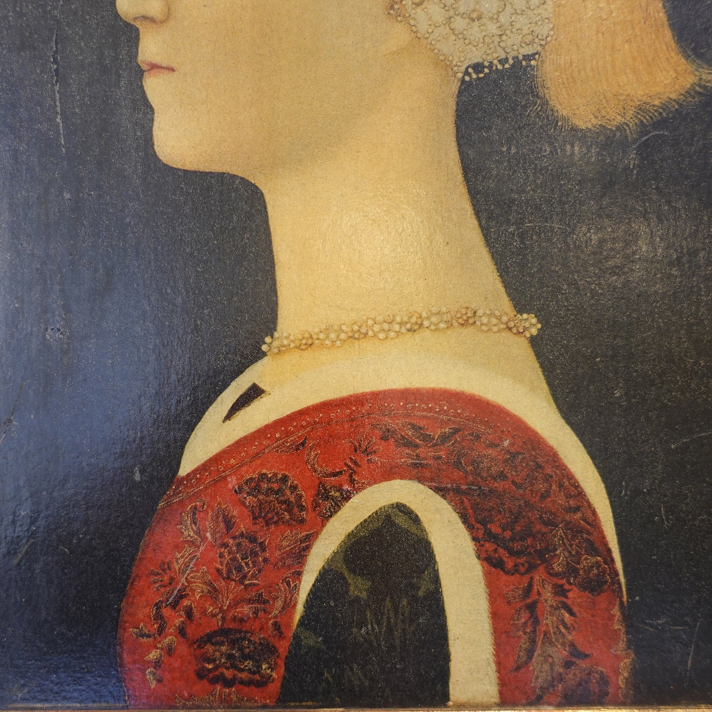 Close-up of a painting showing a person wearing a red garment with intricate patterns.